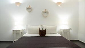 A neatly arranged bedroom with a large bed, two bedside tables, a bedside lamp, a basket, and two wall-mounted light fixtures. - Villa Mare Angelica (Santorini)