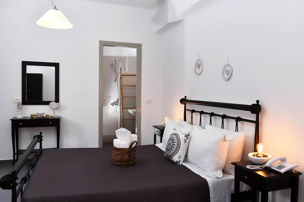 Un dormitorio con cama, mesita de noche, lámpara y espejo.