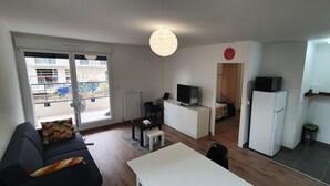Ein kompakter Wohnbereich mit einer Couch, einem Esstisch, einem Fernseher, einem Kühlschrank und einer kleinen Küchenzeile.