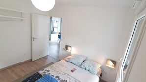Ein Schlafzimmer mit einem Bett, Nachttischlampen, einer Tür und Blick auf einen Flur.