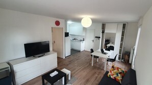 Ein modernes Wohnzimmer mit Flachbildfernseher, einer Couch, einem Esstisch mit Stühlen und einer Küche im Hintergrund.