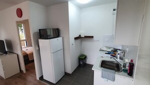Eine kleine Küche mit einer Mikrowelle auf einem weißen Kühlschrank, einem kleinen Spülbecken mit Abtropfgitter und einem Mülleimer.