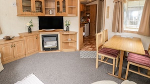 Una habitación compacta y bien iluminada con muebles de madera, televisor, refrigerador pequeño y comedor con mesa y sillas.