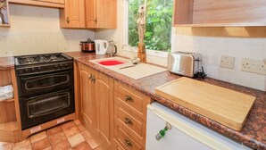 Cocina con armarios de madera, estufa, pileta, tostadora y ventana con vista a follaje.