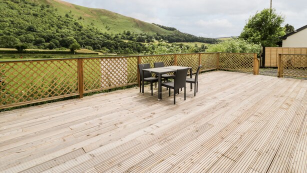 Una terraza de madera con una mesa y sillas, con vistas a un valle verde y colinas.