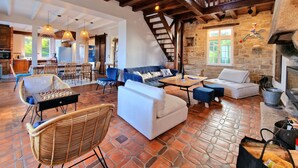 A spacious living area with a fireplace, stone walls, and a mix of seating options including a sofa, chairs, and ottomans. - Dream destination, right by the sea, (Santec)