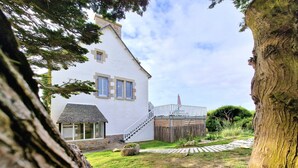 A white house with a stone foundation, a wooden deck, and a stone pathway leading to the entrance. - Dream destination, right by the sea, (Santec)