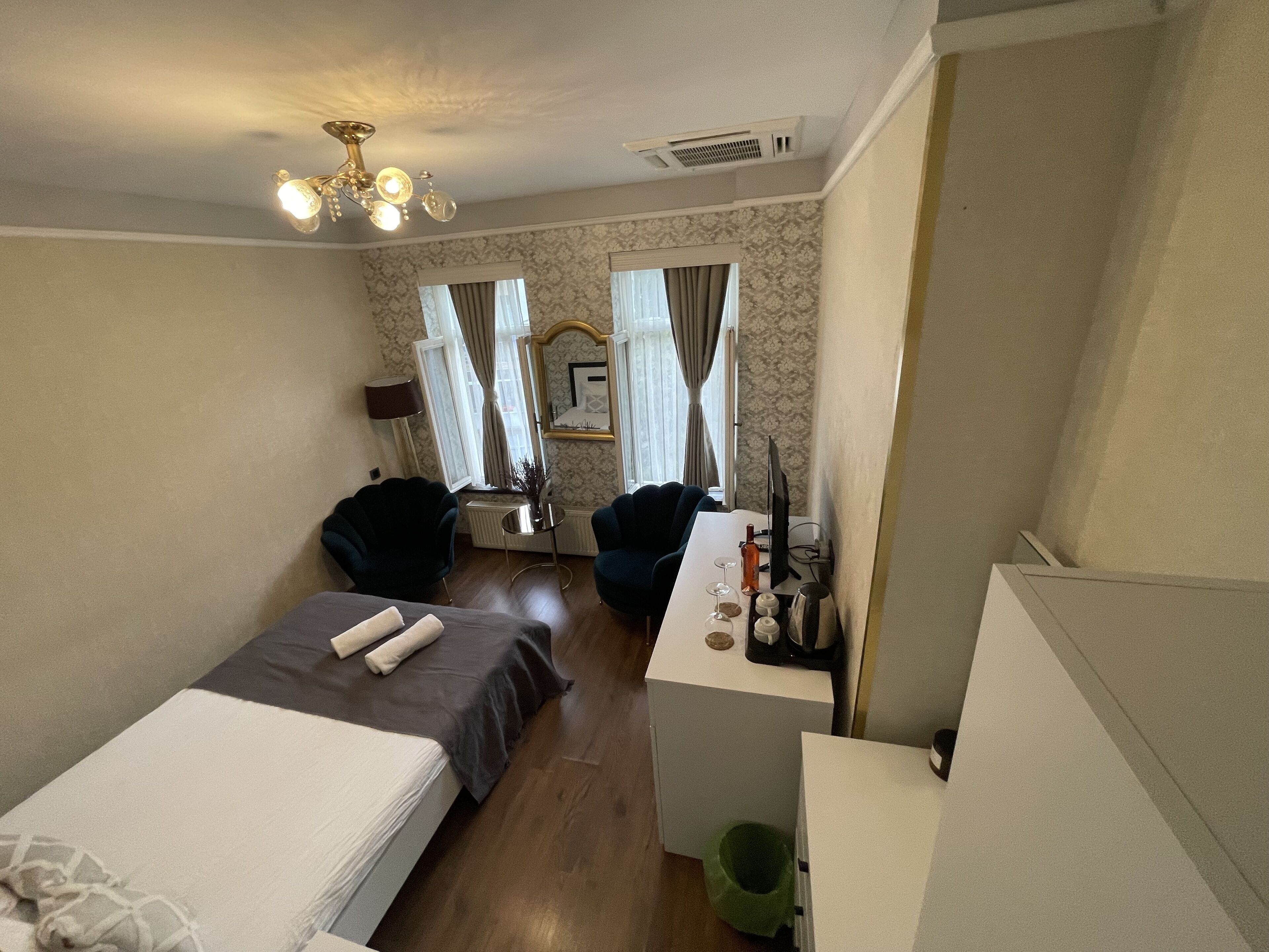 A hotel room with two single beds, a desk with a computer, a chair, and a small table with a bottle and glasses.