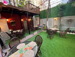An outdoor patio area with a dining table and chairs, surrounded by artificial grass and a wooden deck.