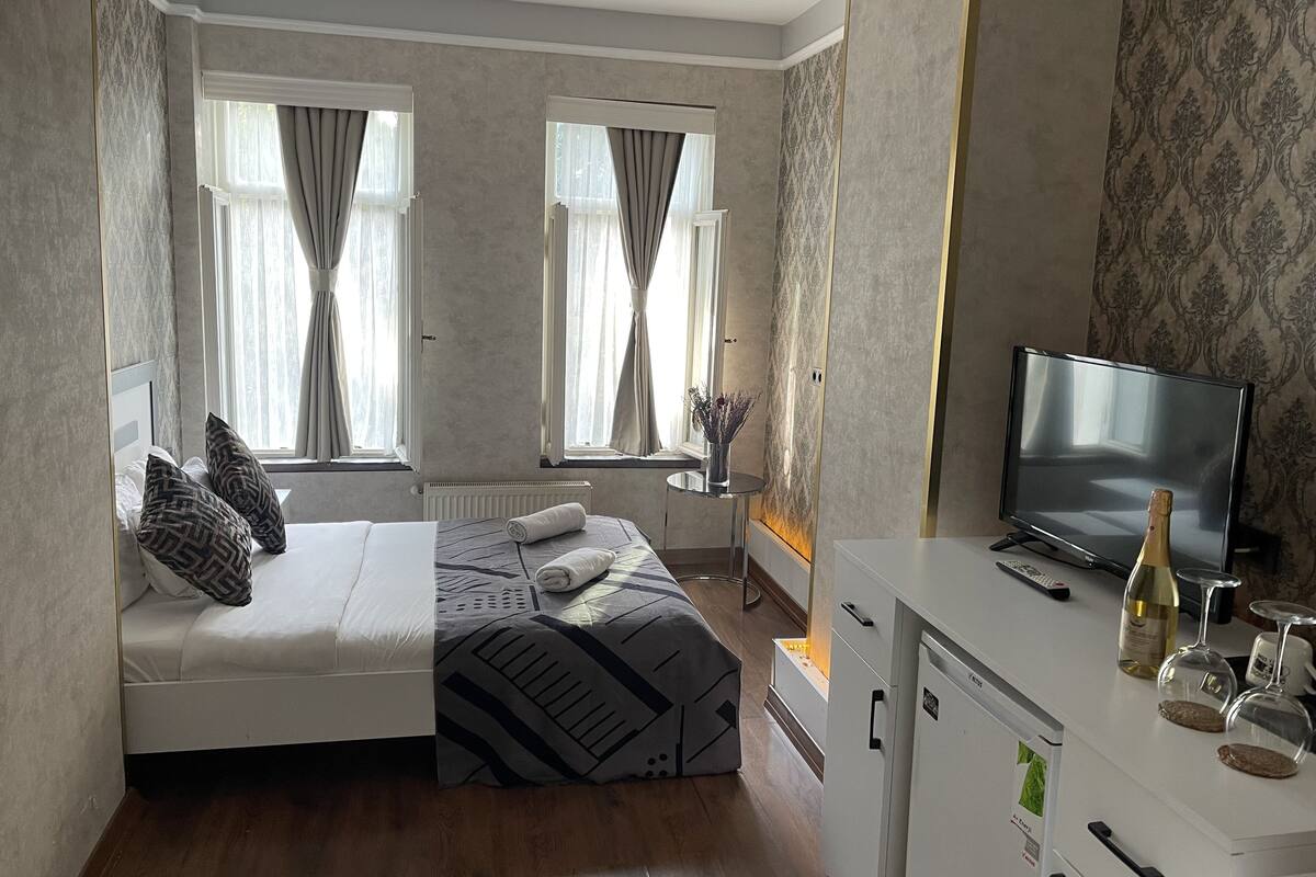 A bedroom with a bed, a television, a minibar, and a window with curtains.