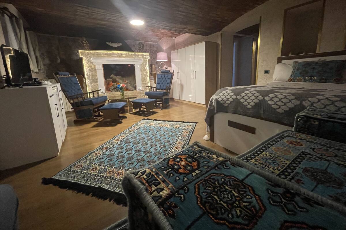 A cozy room with a bed, two armchairs, a small table, and a fireplace.