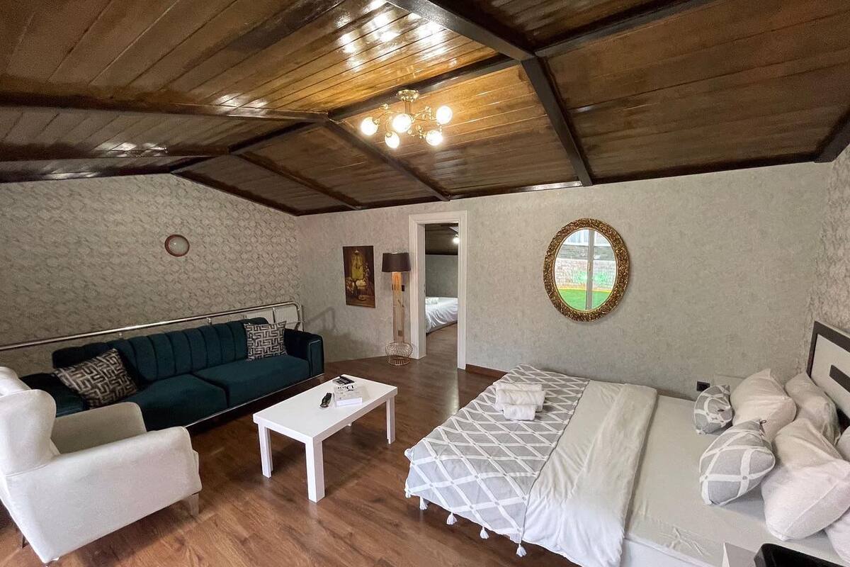 A cozy room with a wooden ceiling, a white sofa, a bed with a patterned bedspread, and a small white table.