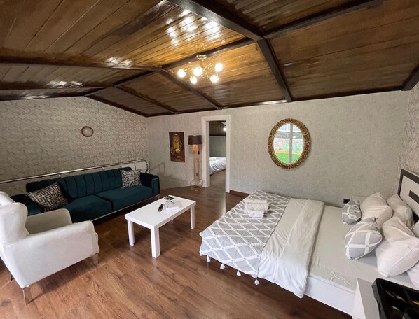 A cozy room with a wooden ceiling, a white sofa, a bed with a patterned bedspread, and a small white table.