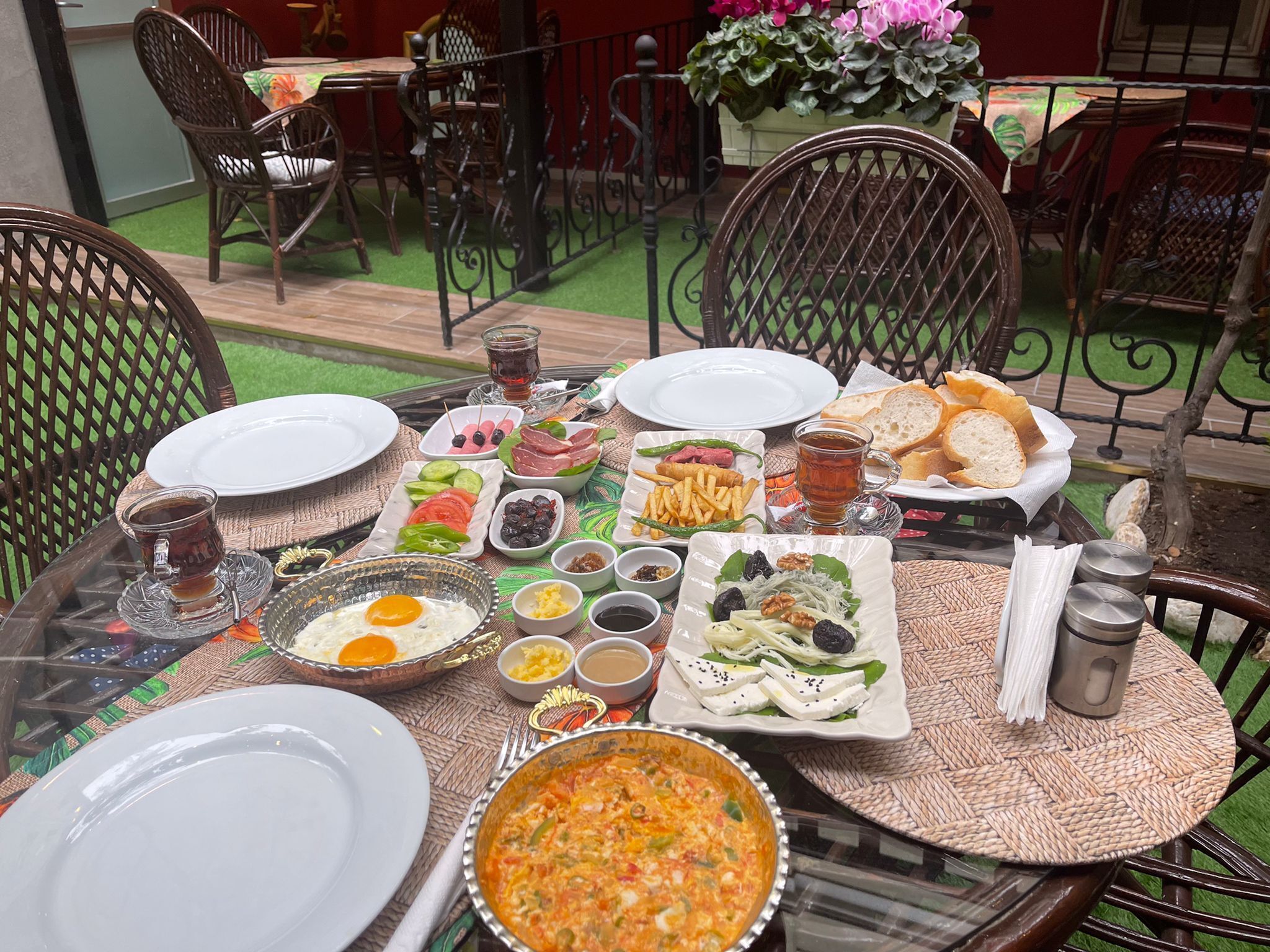 Een tafel gedekt met diverse gerechten, waaronder eieren, salades en brood, omringd door rieten stoelen en een potplant.