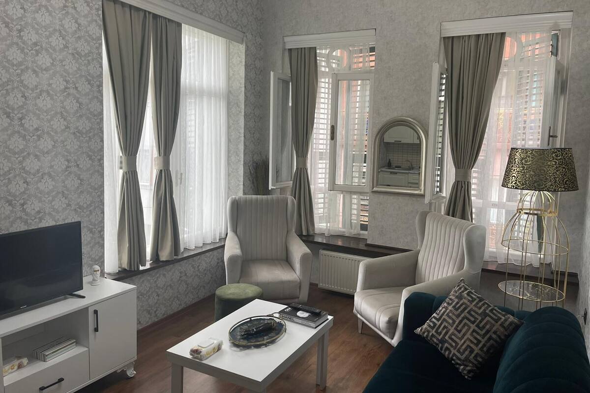 A modern living room with a flat-screen TV, two armchairs, a sofa, a coffee table, and a lamp.