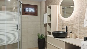 Un baño moderno con cabina de ducha de vidrio, un espejo redondo, un lavamanos con lavabo y un inodoro.