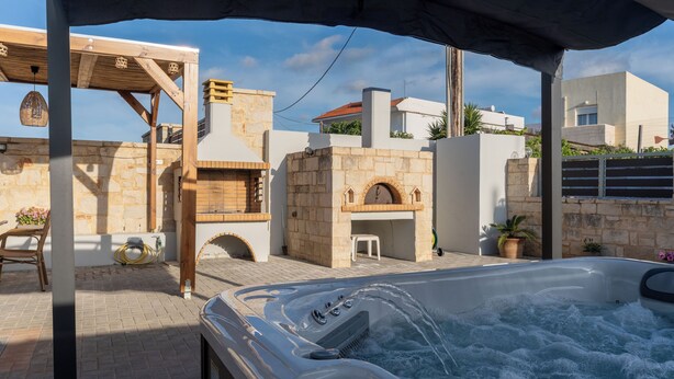Un jacuzzi bajo una pérgola de madera con paredes de piedra y suelo de ladrillo.