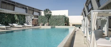 A swimming pool with lounge chairs and umbrellas, surrounded by a modern building with a geometric facade and a vertical garden.