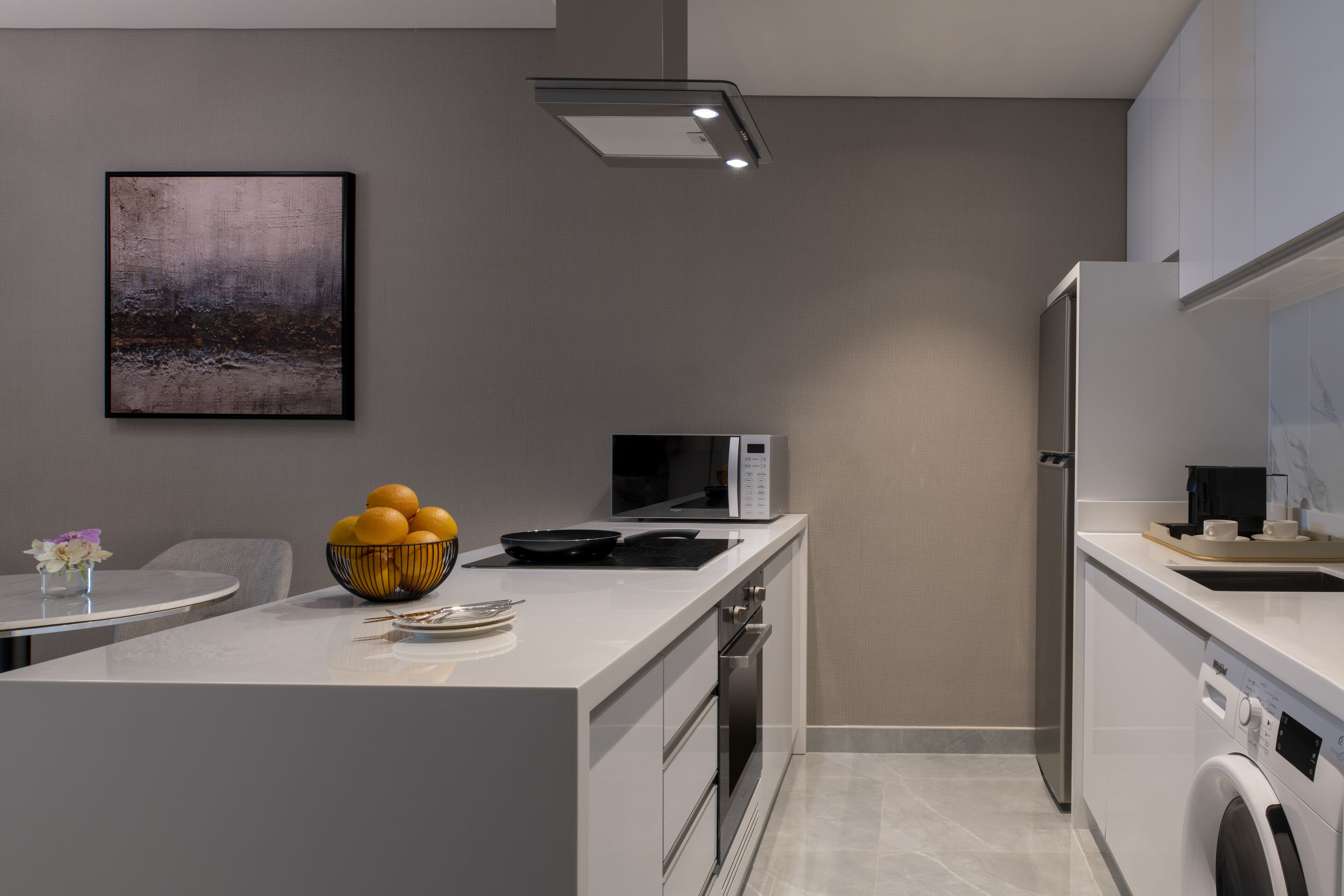 Une cuisine moderne avec un îlot central, un four à micro-ondes, un lave-linge et un tableau accroché au mur.