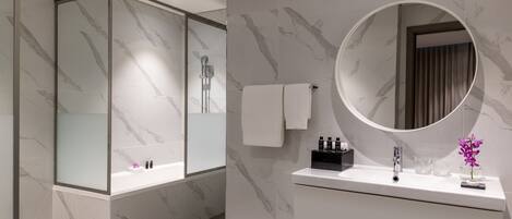 A modern bathroom with a glass-enclosed shower, a round mirror, and a white vanity with toiletries.