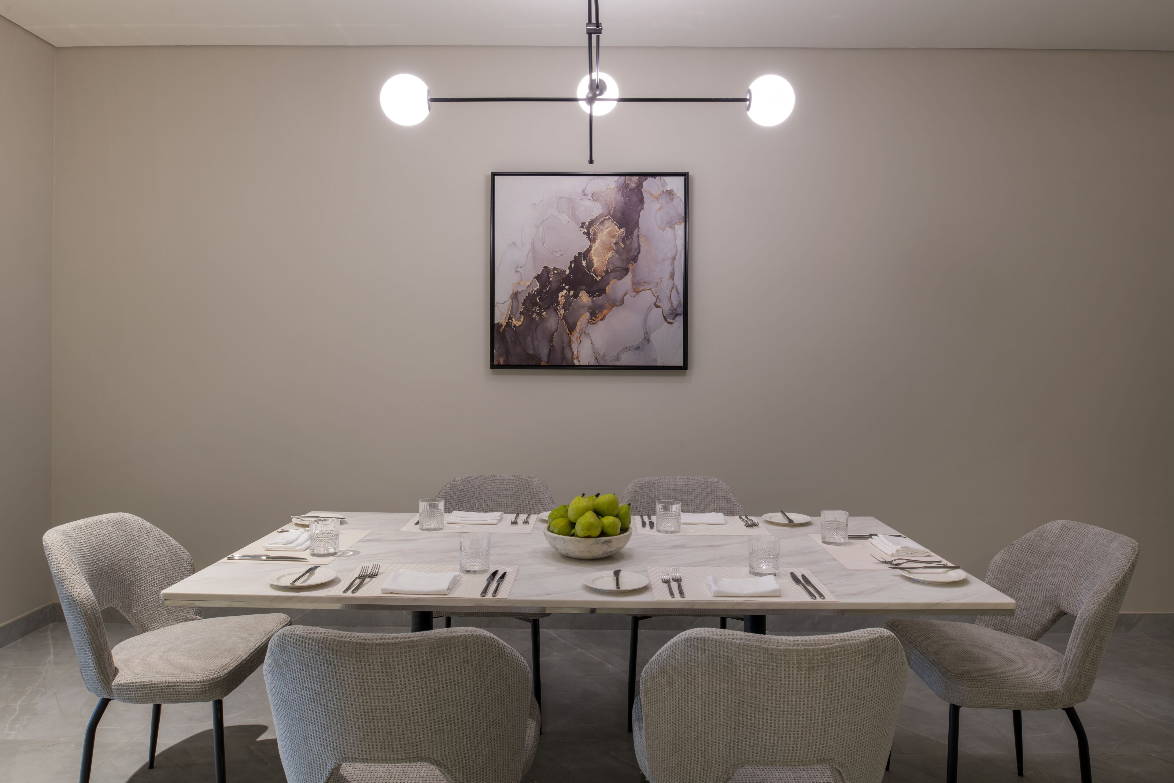 Un comedor con una mesa de mármol, sillas tapizadas en gris y un frutero como centro de mesa.