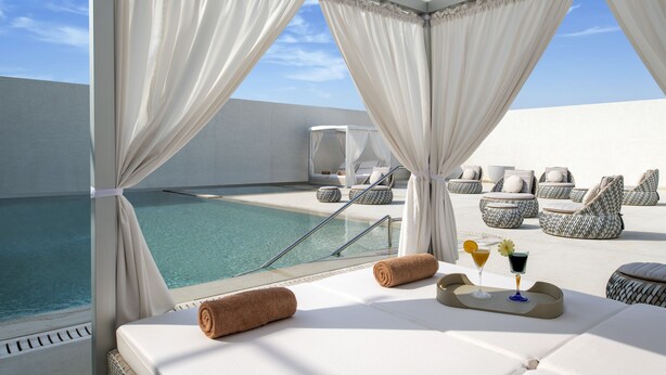 A balcony with a pool, white curtains, and lounge chairs. - Steigenberger Residence Doha (Doha)