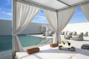 Ein Balkon mit Pool, weißen Vorhängen und Liegestühlen.
