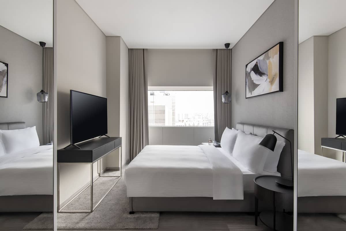 A modern hotel room with two beds, a TV, a desk, and a large window with curtains.