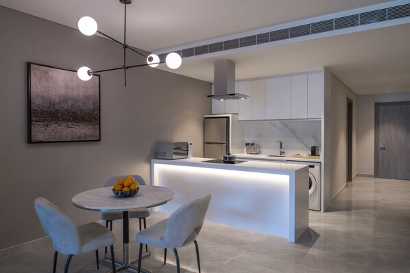 Una cocina moderna con una isla central, una zona de comedor con dos sillas y una lámpara colgante.