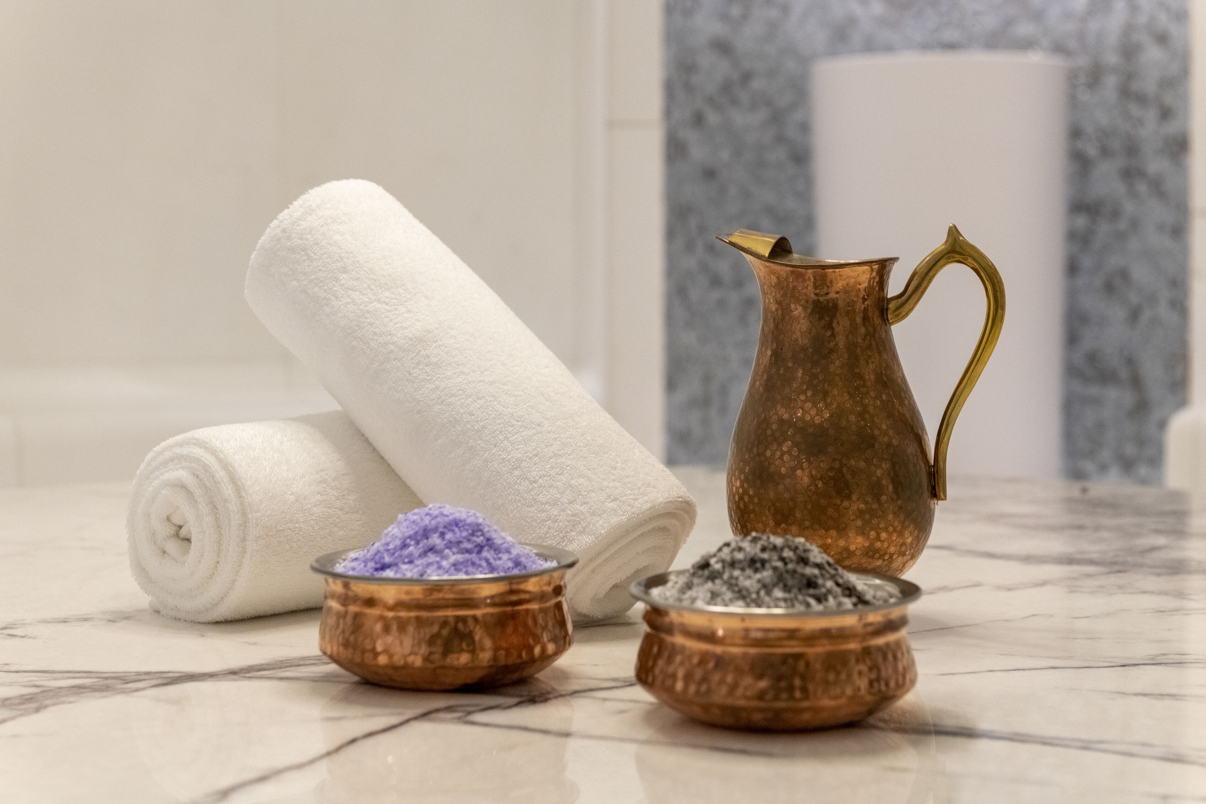 Une salle de bain avec un comptoir en marbre, une serviette blanche et deux récipients en cuivre contenant des sels de bain.