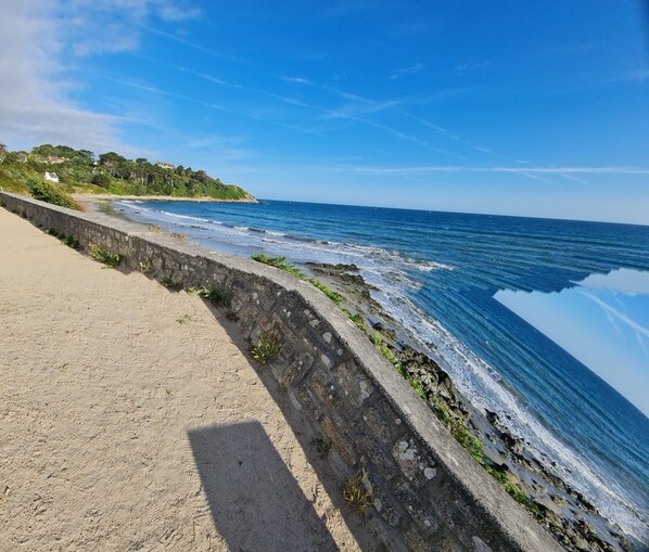 A coastal walkway with a stone wall, leading to a beach with waves crashing onto the shore.