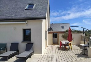 A wooden deck with lounge chairs and a table, a small window, and a door leading to a covered area.