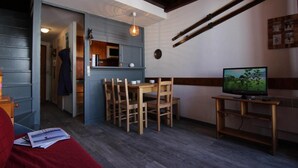 Une pièce chaleureuse avec une table à manger, des chaises, un téléviseur et des paires de skis accrochés au mur.