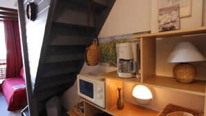Une petite chambre comprenant un lit, un four à micro-ondes, une machine à café et une lampe posée sur une étagère.