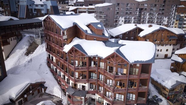 Un hôtel à plusieurs étages doté de balcons, d’un télésiège et entouré d’un paysage enneigé.