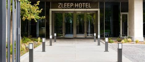 La entrada al Hotel Zleep, con un diseño moderno, cuenta con un frente de vidrio y una señalización clara sobre las puertas.
