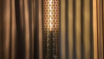 Een cilindervormige lamp met een geperforeerd metalen ontwerp, hangend voor donkere gordijnen.