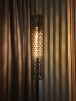 Una lampada cilindrica con decorazioni in metallo forato, sospesa di fronte a tende scure.
