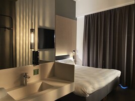 Una camera d'albergo moderna con un letto grande, un lavandino integrato, uno specchio e una TV a schermo piatto.