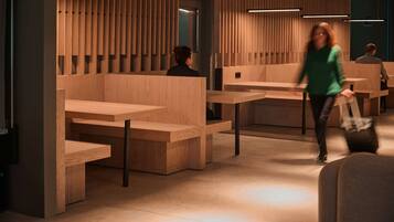 Un interior moderno con separadores y mesas de madera, una persona caminando y otra sentada al fondo.