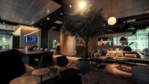 A modern lounge area with a large tree, seating arrangements, a bar, and a television screen. - Zleep Hotel Madrid Airport (Madrid)