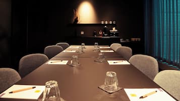 Una sala de conferencias con una larga mesa, sillas, un control remoto y una cortina azul de fondo.