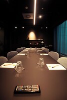 Una sala conferenze con un lungo tavolo, sedie, un telecomando e una tenda blu sullo sfondo.
