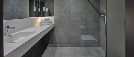 A modern bathroom with a large mirror, two sinks, a toilet, and a shower area.