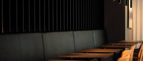 L’intérieur d’un restaurant présente des tables et des chaises en bois foncé, un éclairage suspendu et un mur noir orné de lattes verticales.