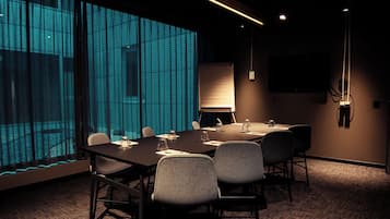 Un salón de conferencias con una gran mesa, sillas, una pizarra y una pantalla de televisión.