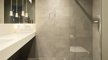 Un baño moderno con un espejo grande, dos lavamanos, una ducha con puerta de cristal y lámparas colgantes.