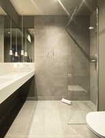 Ein modernes Badezimmer mit einem großen Spiegel, zwei Waschbecken, einer Dusche mit Glastür und hängenden Pendelleuchten.