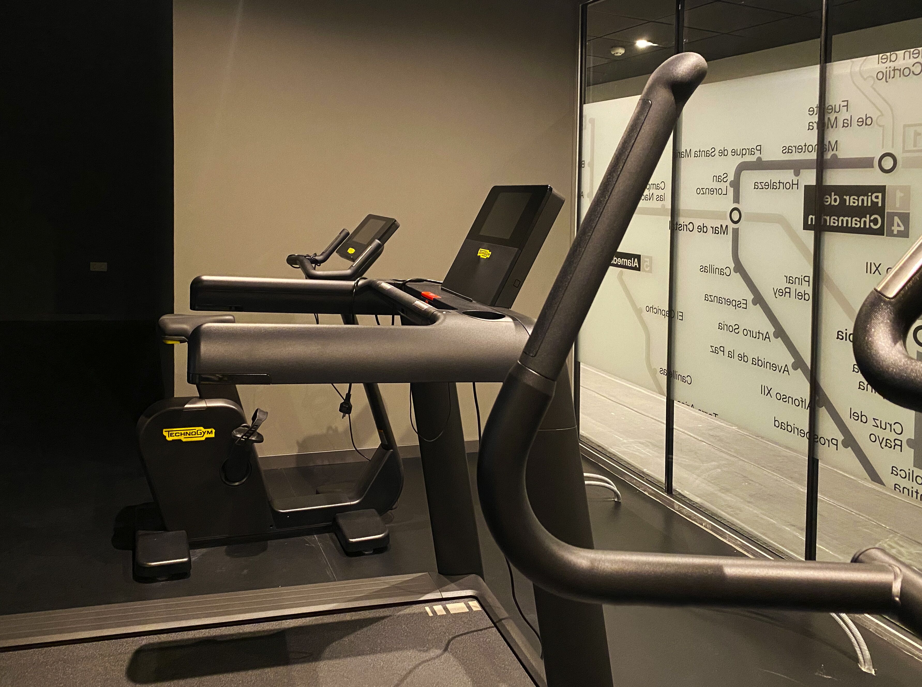 Un gimnasio con cintas de correr y una bicicleta estática, una pared con un mapa, y una puerta con manija.