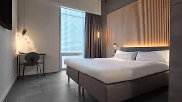 Una habitación de hotel moderna con una cama grande, un escritorio y una silla. Hay una ventana con cortinas, una lámpara de pared y un televisor en la pared.